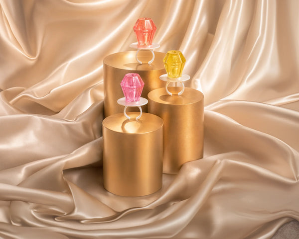 Three gold cylindrical pedestals arranged on draped champagne satin, each holding a Ring Pop® candies