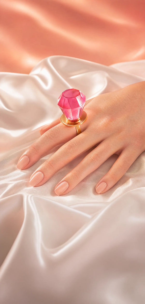 A hand wearing a Ring Pop®, resting on draped white satin fabric with a soft peach background.